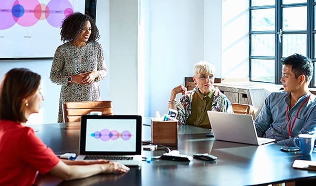 Woman stands at head of table where three other people sit