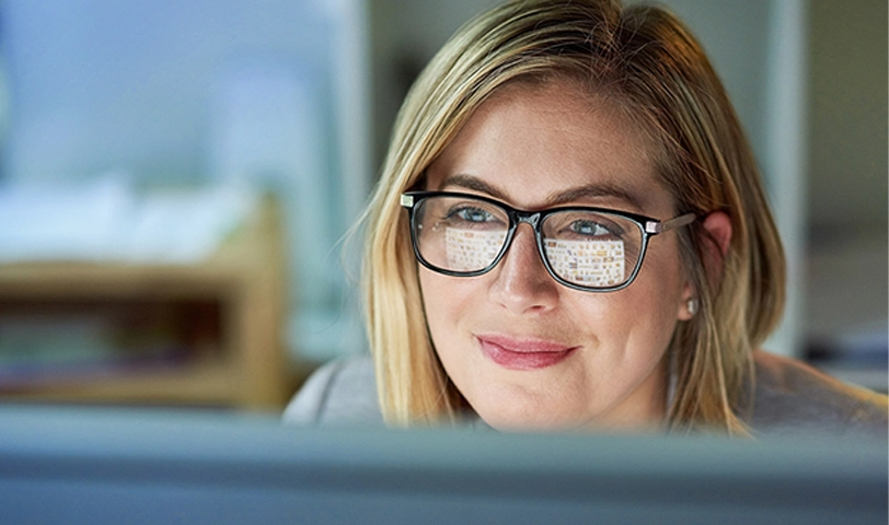 Woman sits behind computer. The screen reflects in her glasses.