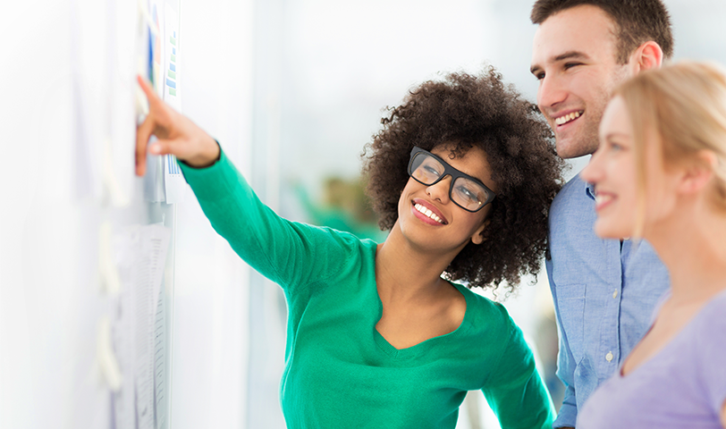 Woman points at board while another man and woman stand next to her