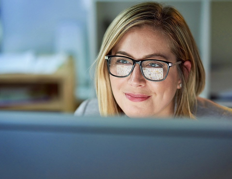 Woman sits behind computer. The screen reflects in her glasses.