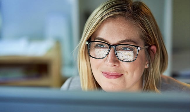 A woman in glasses sits behind a computer