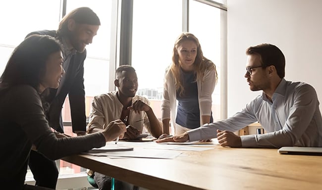 A team of 5 people sits around a table in discussion