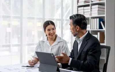 A coach and coachee engage in a focused discussion at an office table with a tablet and papers, reflecting the impact of working with one of the best executive coaching companies, Right Management.
