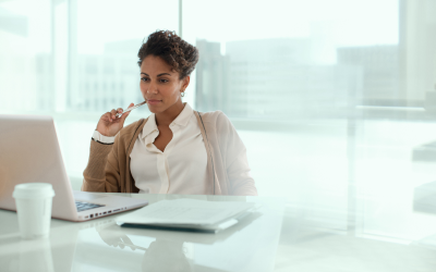 A woman sits at her desk in a modern office, focused on her laptop as she completes a psychometric test for an executive leadership assessment.