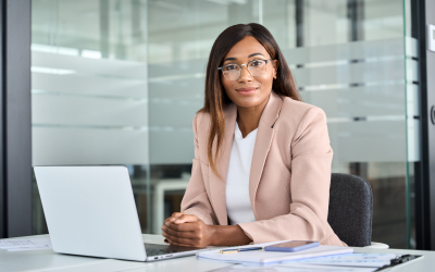 A confident female leader at a cutting-edge tech firm sits in her office, laptop open, embodying her company's talent management strategies designed to foster female leadership and drive innovation.