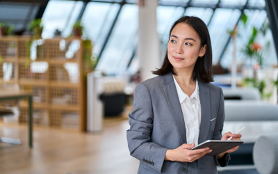 A confident leader stands alone in a modern office, tablet in hand, showcasing the impact of a Right Management leadership development program on her growth.