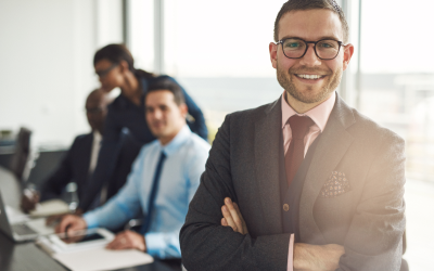 A young, emerging, high-potential leader stands confidently in a conference room, with three colleagues behind him, reflecting the high impact of Right Management's leadership development programs. 