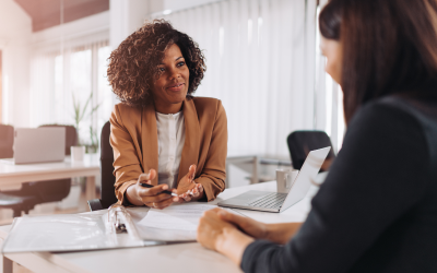 A Right Management coach sits at a table in an office with her laptop open, providing career development coaching to an Operation HOPE client. This session is part of their collaborative initiative aimed at empowering individuals and communities nationwide.