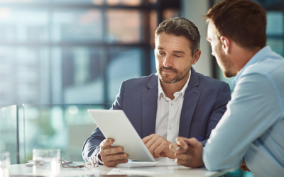 Two HR professionals sit at a table in a modern office, discussing a reduction in force while using a tablet to explore outplacement services for a smoother transition.