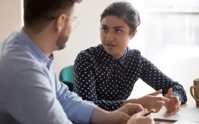 A coach and coachee sit next to each other during a one-on-one coaching session, with a coffee cup nearby. The session is part of the company’s outplacement program, reflecting its commitment to corporate and social responsibility. 
