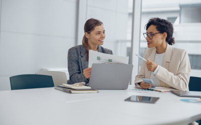A coach and a coachee discuss career options as part of an outplacement program in a modern office setting. The company carefully considered how to support employees during layoffs, deciding that outplacement would benefit both departing and remaining staff, as well as the organization overall. This thoughtful conversation highlights the success of their strategy.