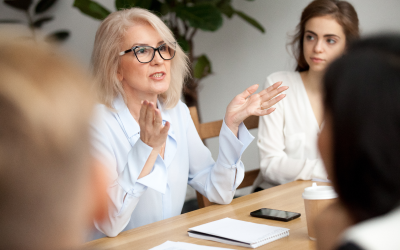 A senior executive sits at a conference table, confidently explaining the company's new strategy to her team. Her leadership and communication skills were honed through a leadership assessment test, identifying her as a high-potential candidate and guiding her leadership development. 