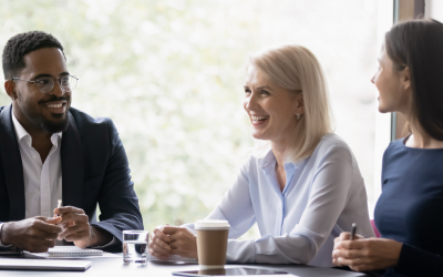 A group of smiling financial services professionals sits around a conference table, actively engaged in discussion. Their company addressed the question of how to prevent employee burnout by implementing talent management solutions. This has fostered a positive work culture as depicted in this image. 