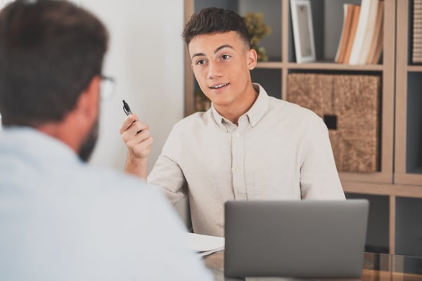 A professionally dressed coach and coachee sit across a table, engaged in a one-on-one coaching session. The coachee, holding a pen with a laptop open in front of them, receives guidance as part of the company's career transition services for employees impacted by layoffs.