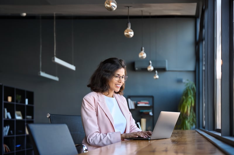 A professionally dressed individual takes a leadership assessment on their computer in a modern office environment. 