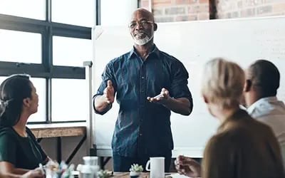 A man who completed executive leadership coaching presents to a group in a business setting.